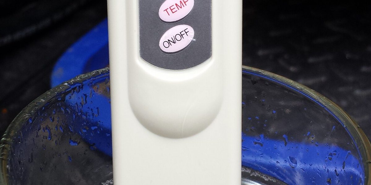 Digital TDS meter dipped in a glass of water showing a reading in ppm