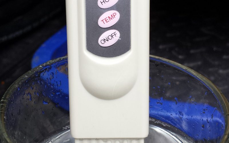 Digital TDS meter dipped in a glass of water showing a reading in ppm